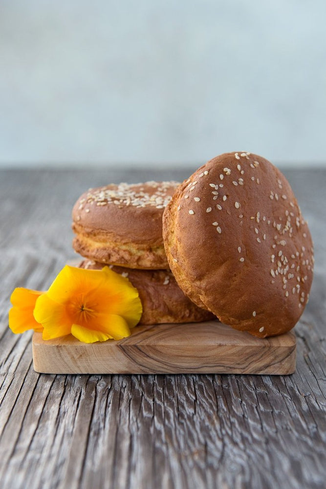 
                      
                        pile gluten free hamburger buns with sesame seeds on wood board with flowers
                      
                    