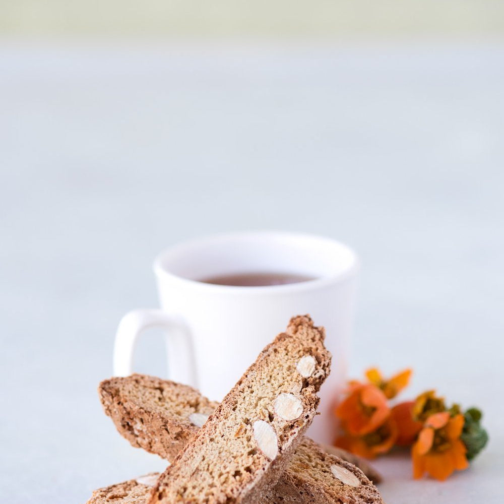 stack of 3 gluten free candied orange almond biscotti in front of cup of tea